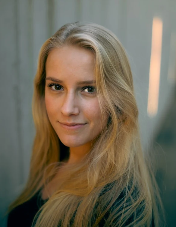 Portrait of a woman with long blonde hair in front of a grey concrete wall.