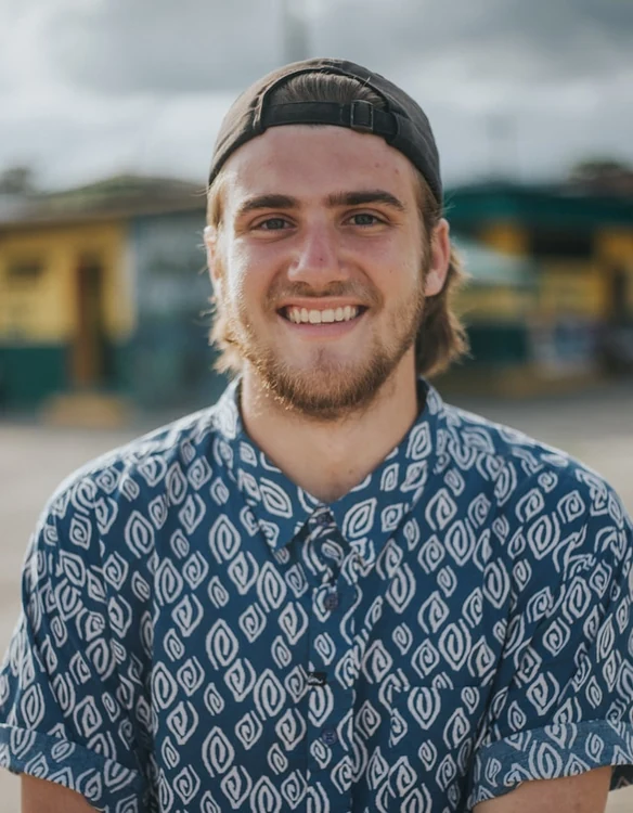 Portrait of a young man in a patterned shirt and backwards cap smiling outdoors.