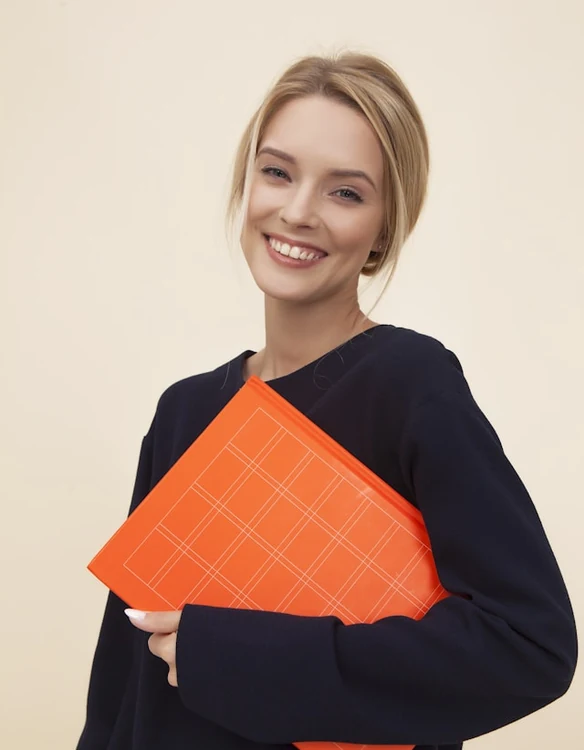 Portrait of a woman in a navy sweater holding an orange ring binder.